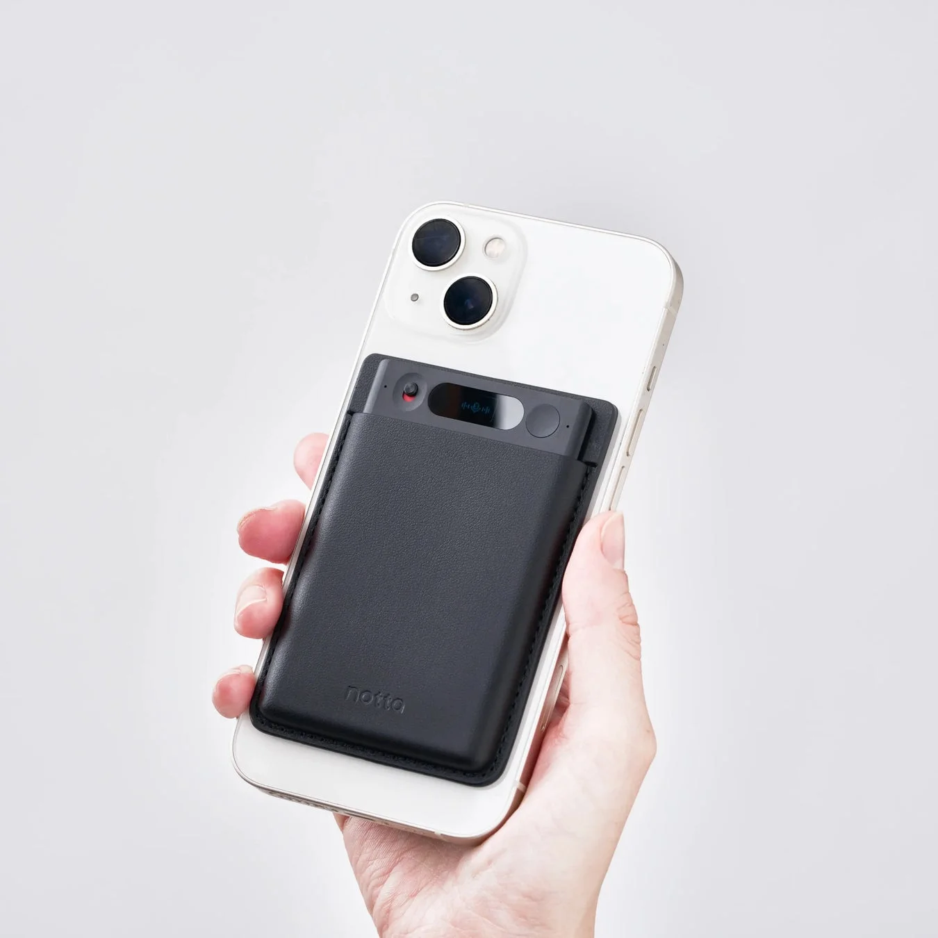 白いiPhoneの背面に、黒いレザー製のスマートウォレット「notta」が取り付けられている様子