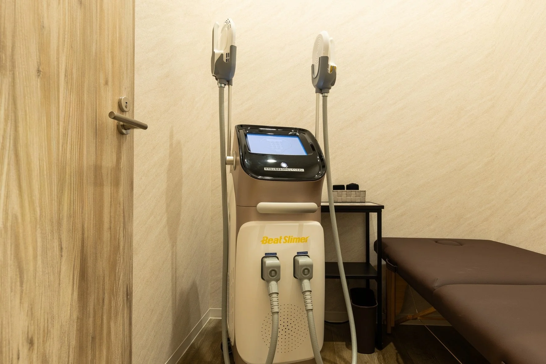 エステサロンの施術室に設置された痩身マシン「Beat Slimer」と、施術用のベッドが写っています。清潔感のあるモダンな空間で、美容クリニックやエステティックサロンの一室を思わせる画像です。