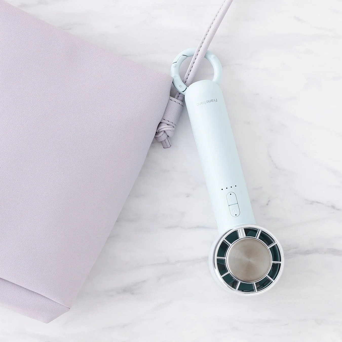 淡い水色のハンディファンと薄紫色のバッグが白い大理石の上で撮影されています