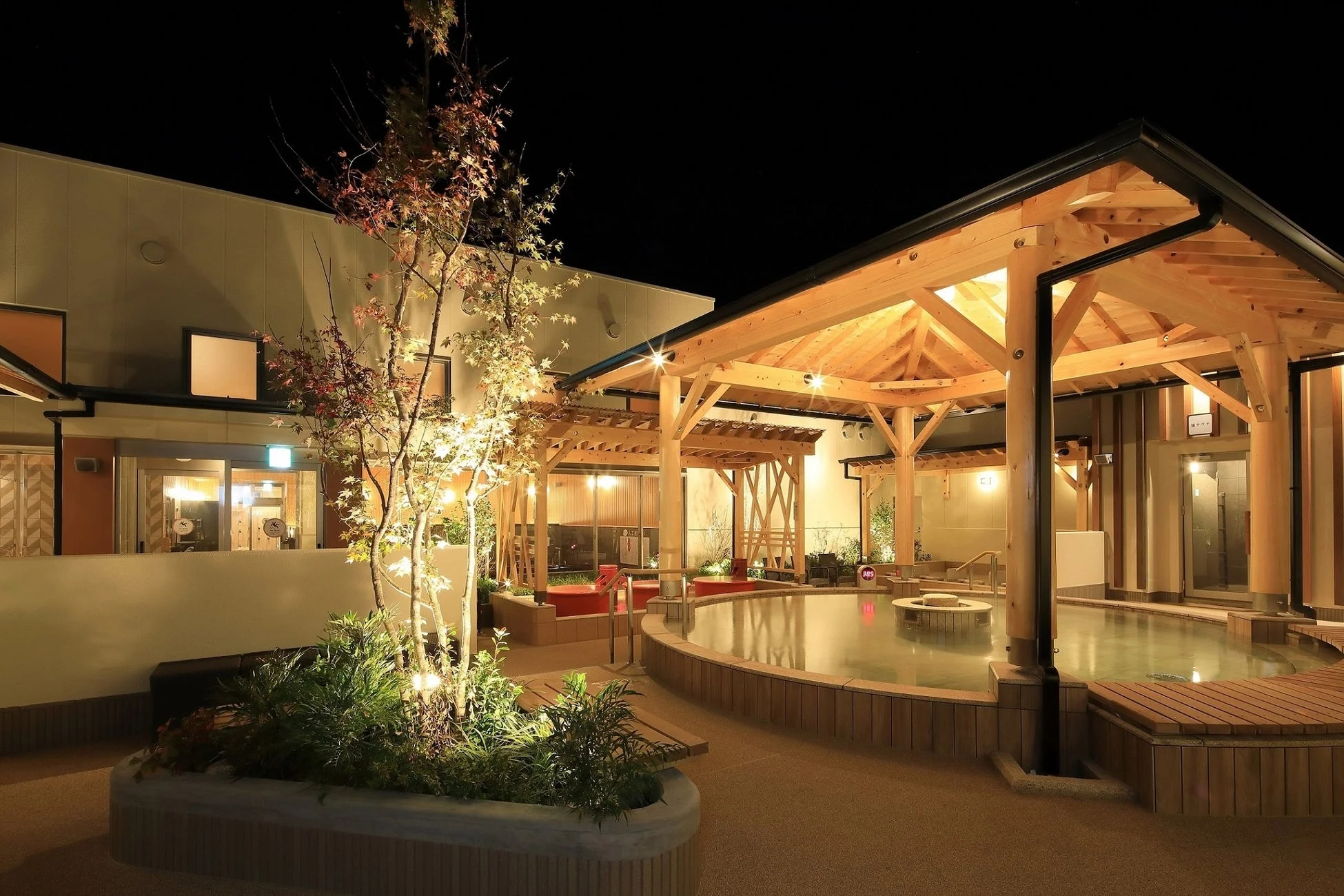 夜の露天風呂の風景。温かい光に照らされた木造の屋根と水面が美しい