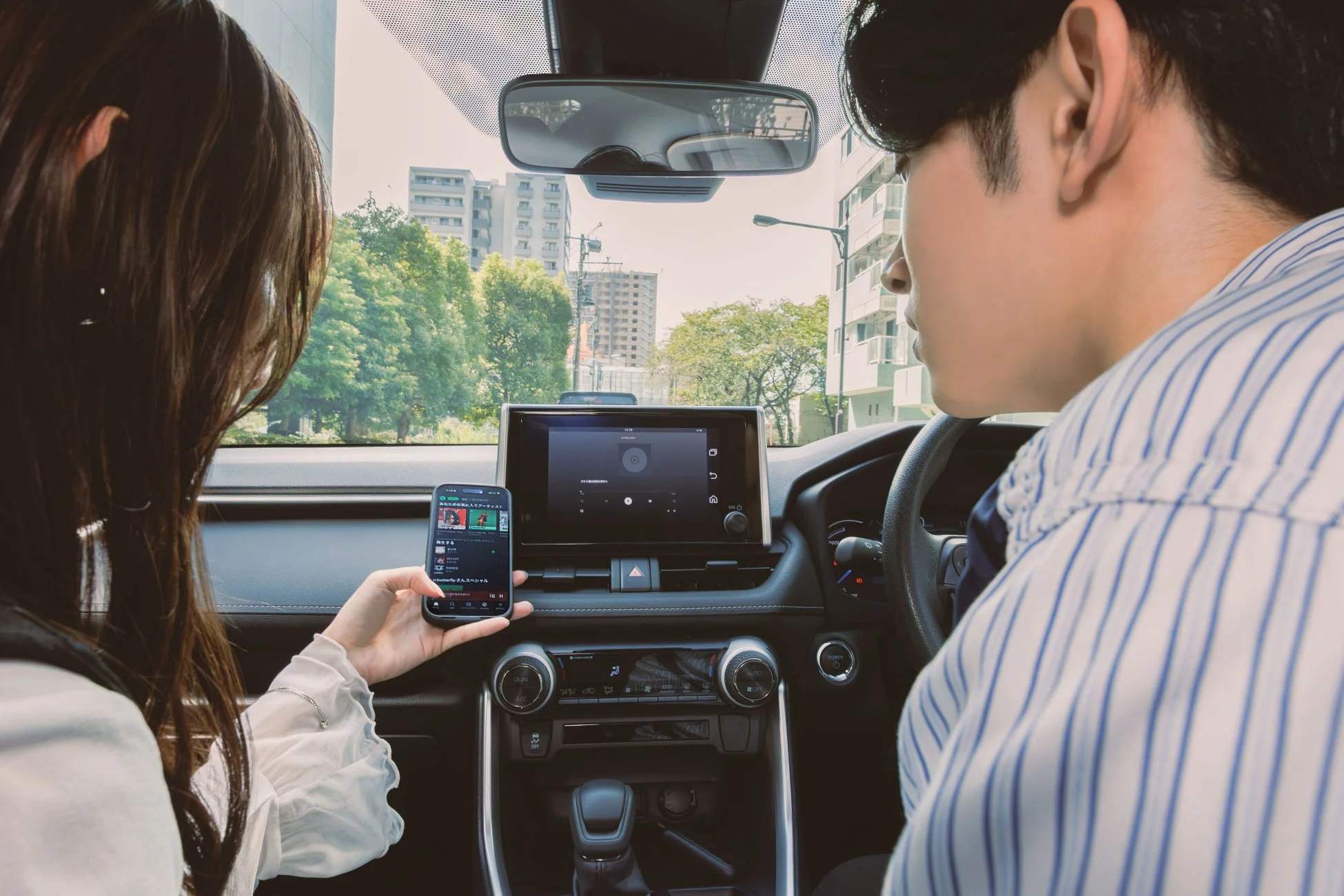 車内でくつろぐカップルがスマートフォンを操作し、カーナビ画面を確認している様子