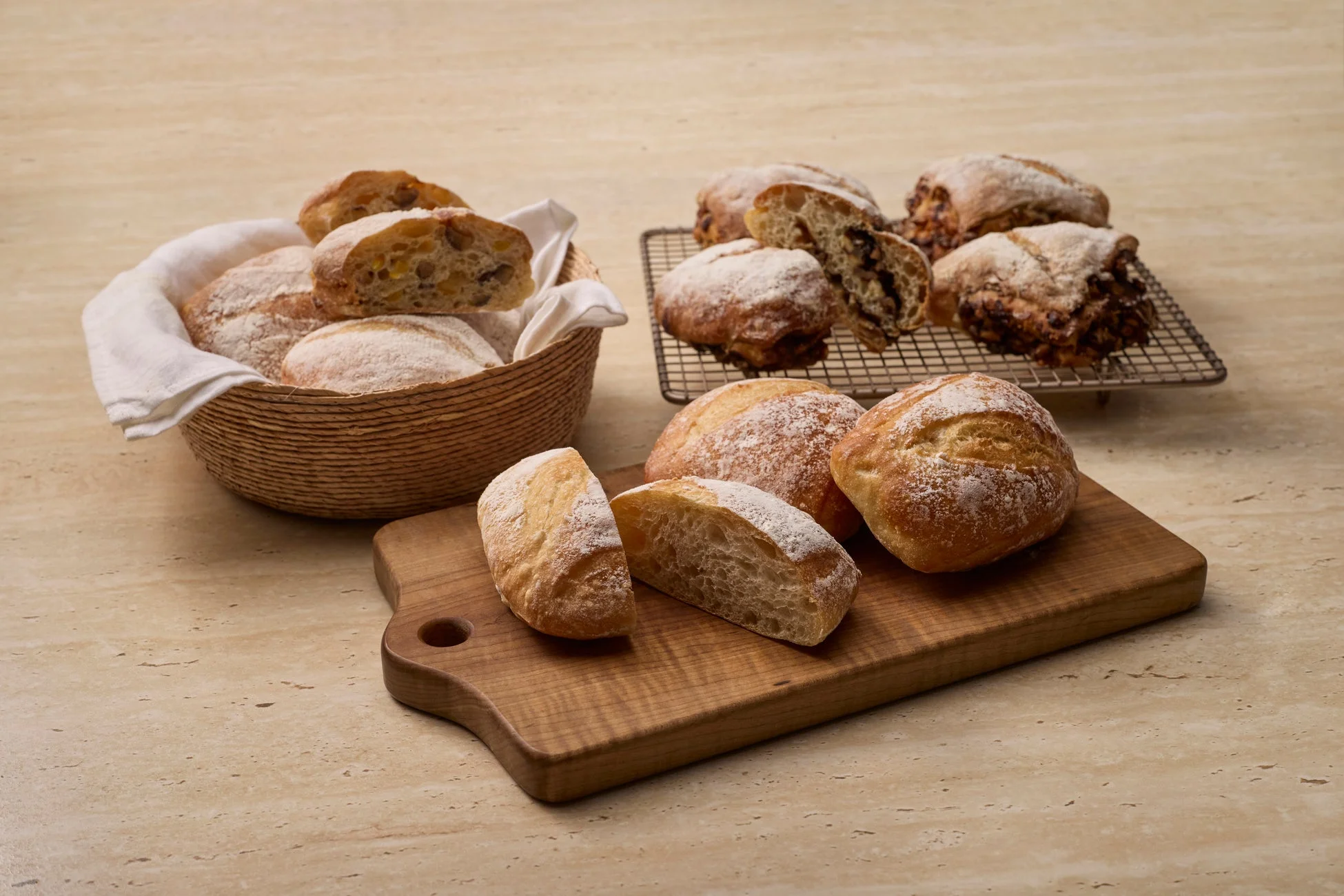 様々な種類の焼きたてのパンが、バスケット、冷却ラック、カッティングボードに並べられています