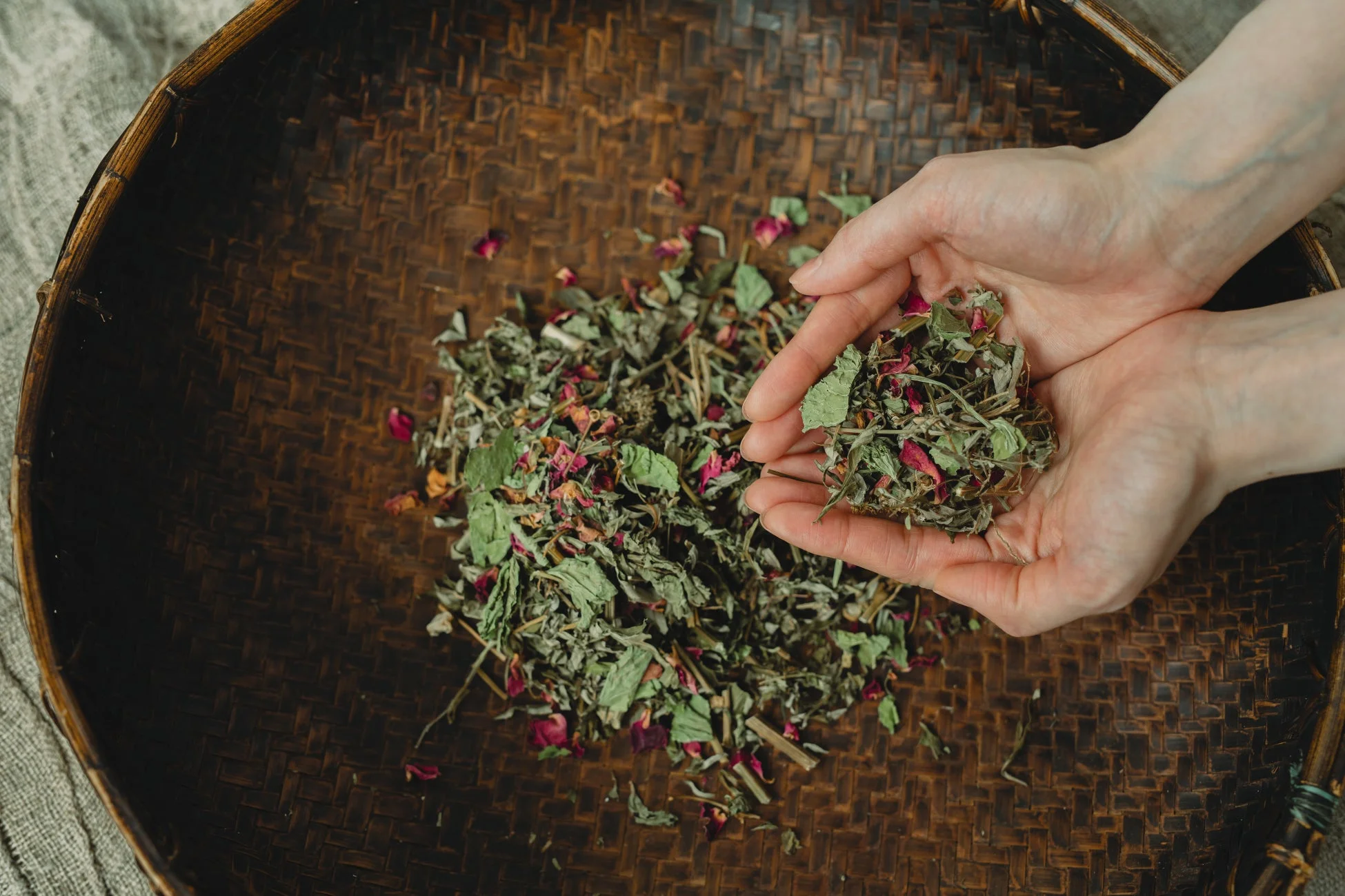 竹籠の上でハーブと花びらの混合物をすくう手元