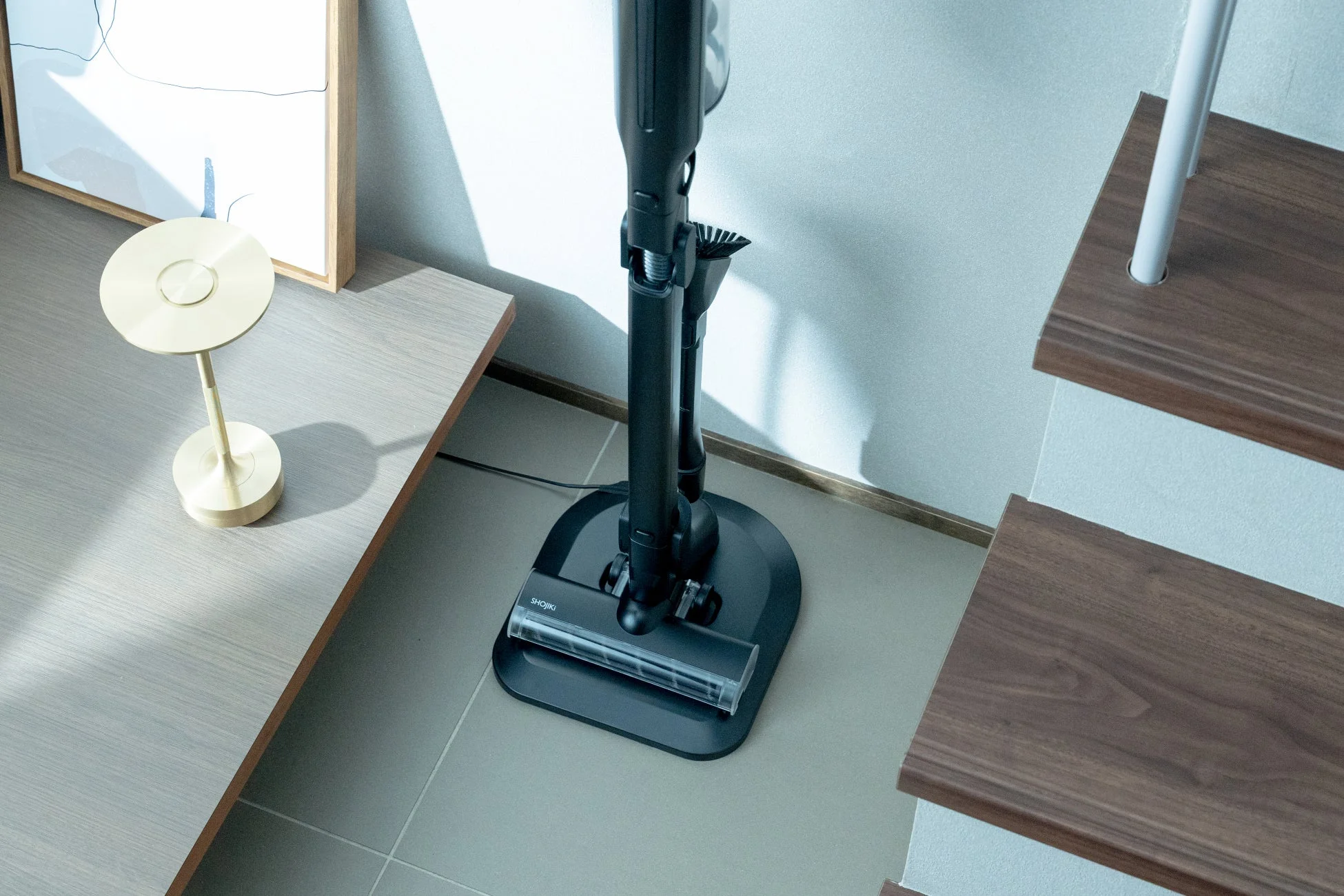 モダンなリビングスペースに置かれた黒いスティック型掃除機が充電スタンドに立てられている