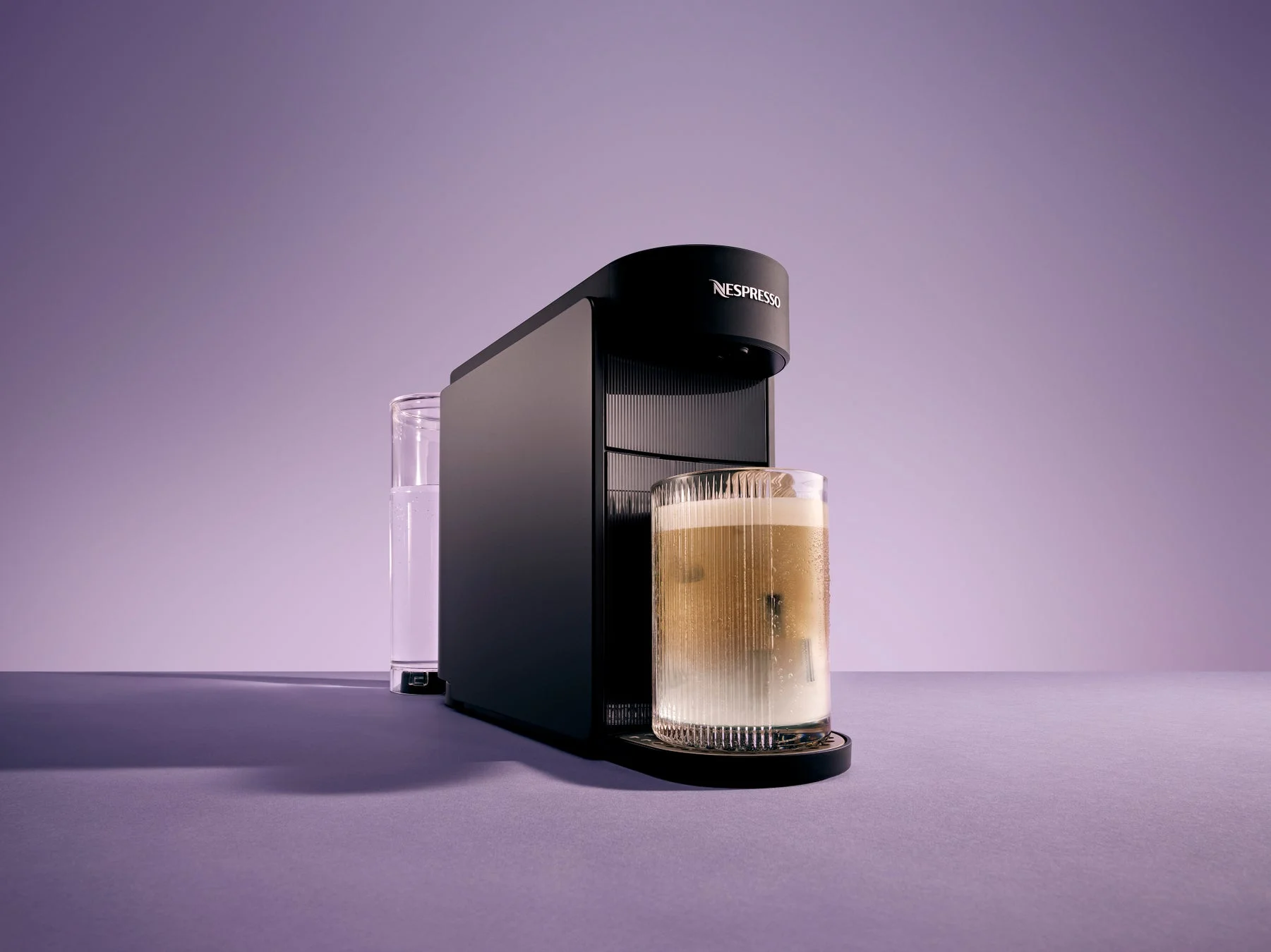 紫色の背景に、ネスプレッソコーヒーメーカーがグラスにコーヒーを抽出している様子