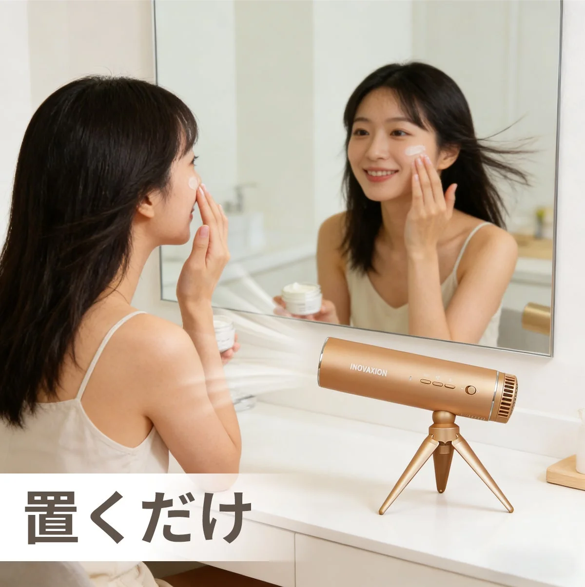 鏡の前でスキンケアをする女性と、カウンターに置かれたゴールズカラーのハンズフリー美容デバイス