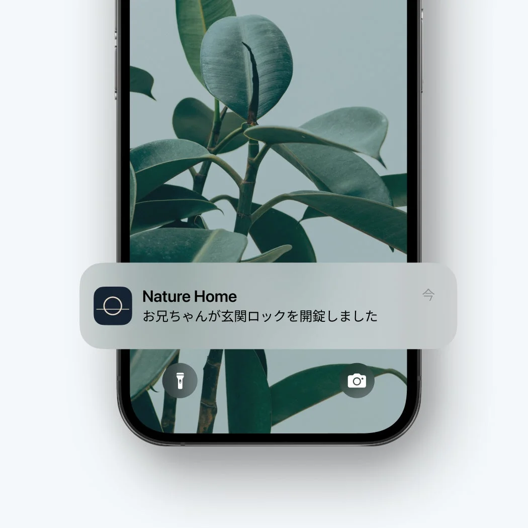 iPhoneのロック画面にスマートホームアプリ「Nature Home」からの通知が表示されています。通知内容は「お兄ちゃんが玄関ロックを開錠しました」で、背景には観葉植物の壁紙が見えます。