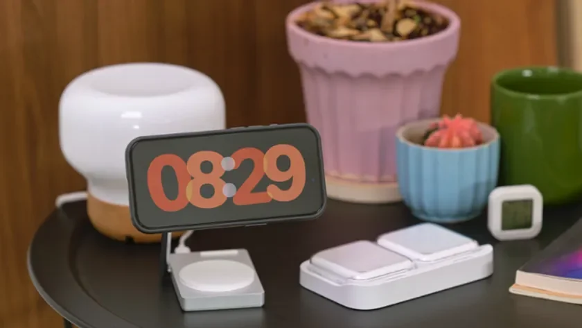 ベッドサイドテーブルに置かれたスマートフォンが「08:29」と表示されています。卓上ライト、植木鉢、充電器などのガジェットが並び、朝の穏やかな雰囲気を醸し出すインテリア