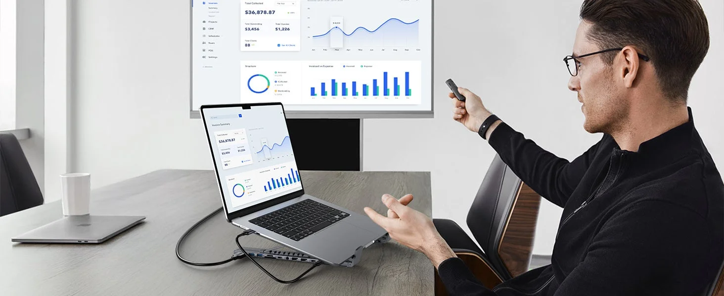 男性がプレゼンテーションを行っており、ラップトップと大型モニターにビジネスデータやグラフが表示されている様子