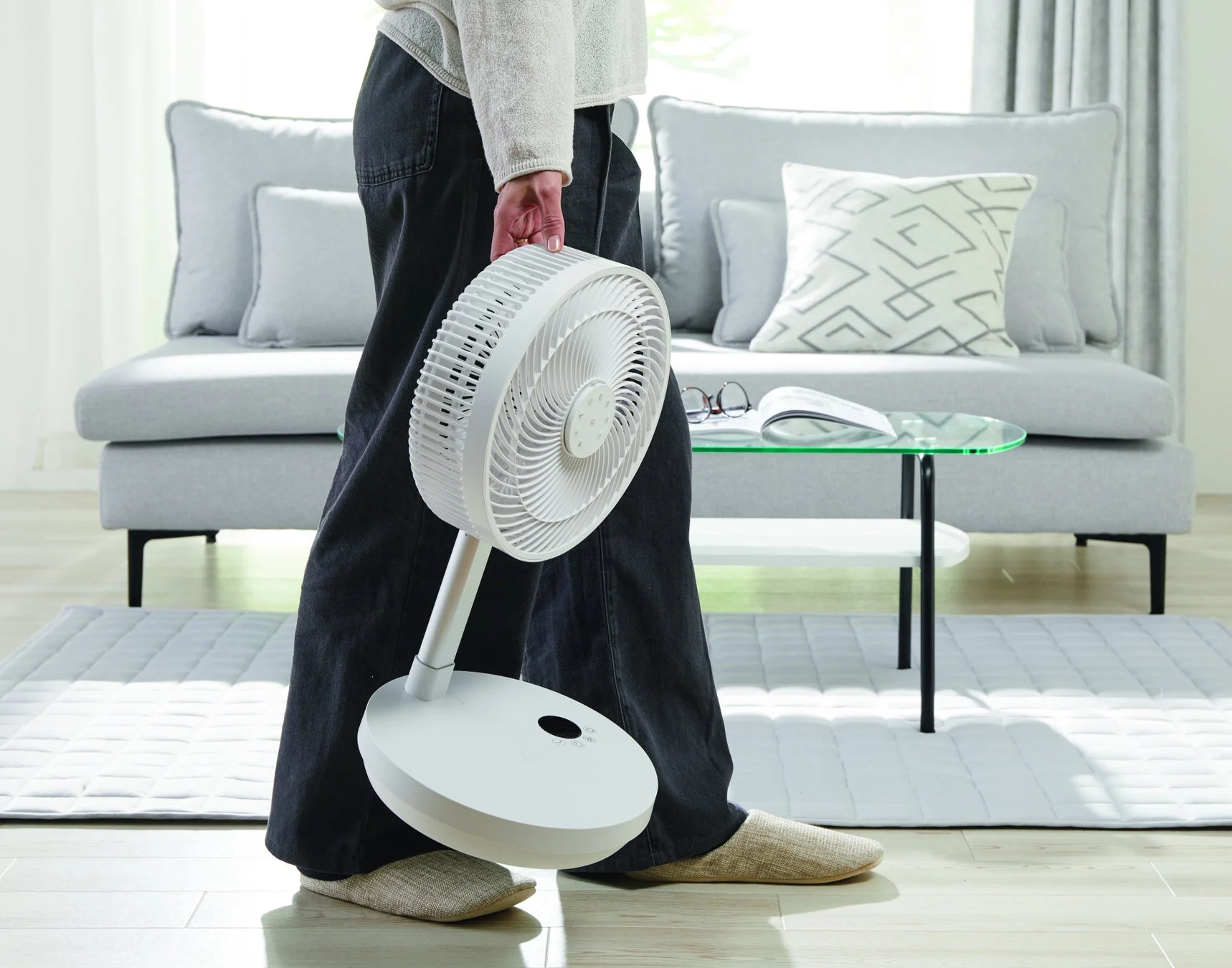 モダンなリビングルームで、一人の人物が白いポータブル扇風機を手に持っています