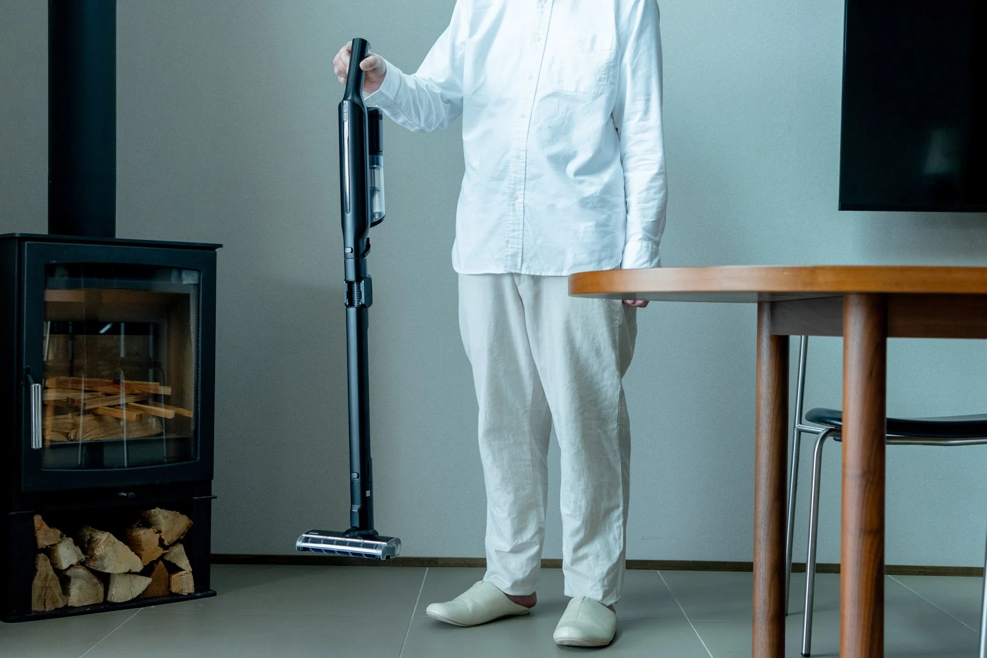 白いシャツを着た人が、モダンなリビングで黒いコードレス掃除機を持っている