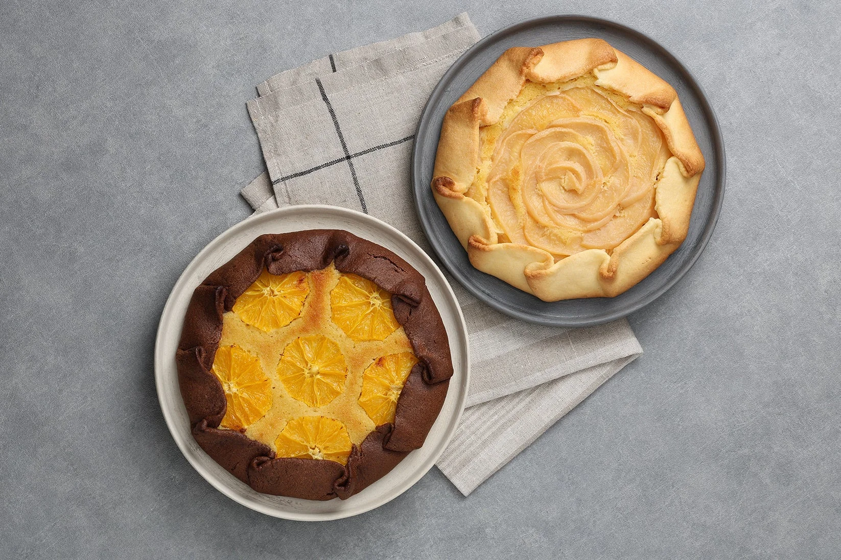 グレーの背景に、チョコレート生地にオレンジ、プレーン生地にリンゴ（または洋梨）が乗った2種類のガレットが並べられています