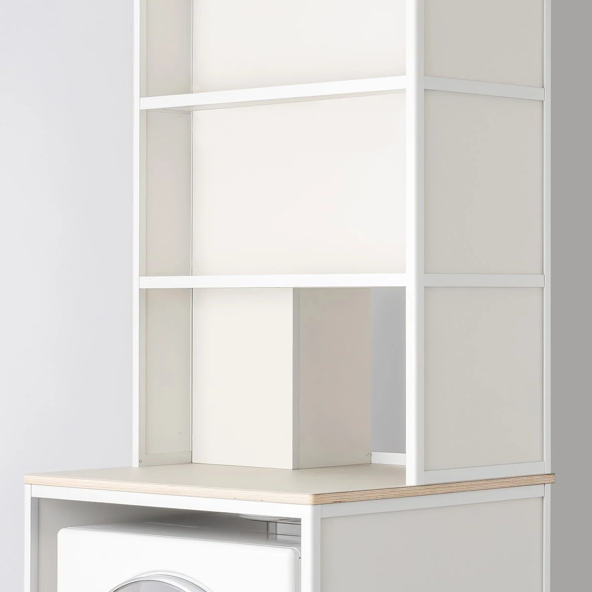 白いフレームと棚板で構成されたシンプルな収納棚の画像です。下部には木目のカウンタートップがあり、その下に白い家電製品の一部が見えています。