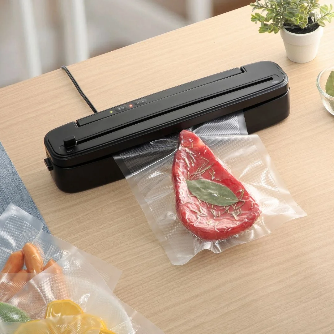 木目調のテーブルで黒い真空パック器が使用されており、ハーブを添えた生の肉が真空パックされています。