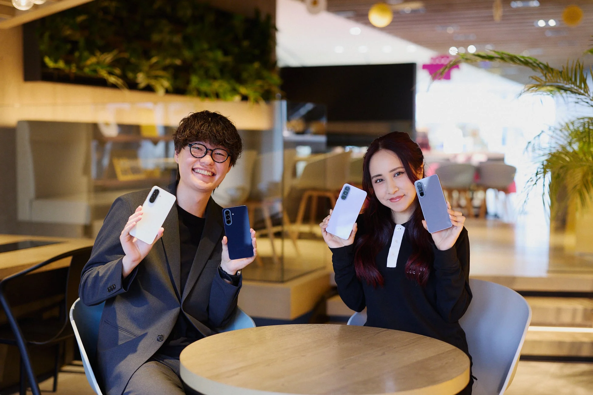 カフェで笑顔の男女が複数色のスマートフォンを持つ様子