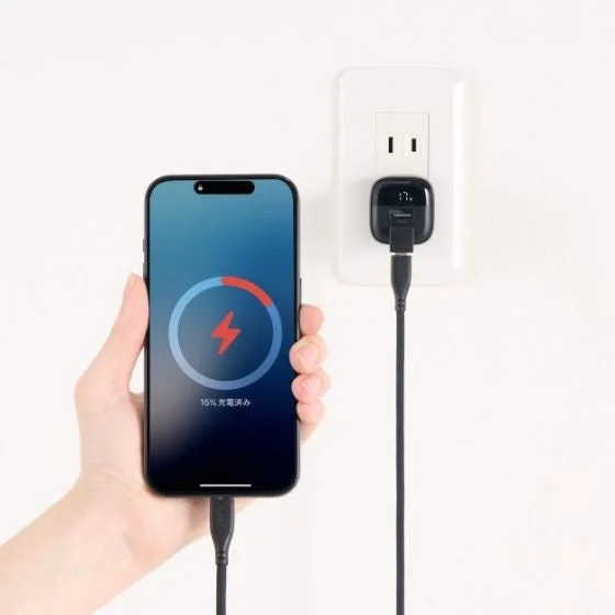 白い壁のコンセントに接続された充電器でスマートフォンが充電されている様子
