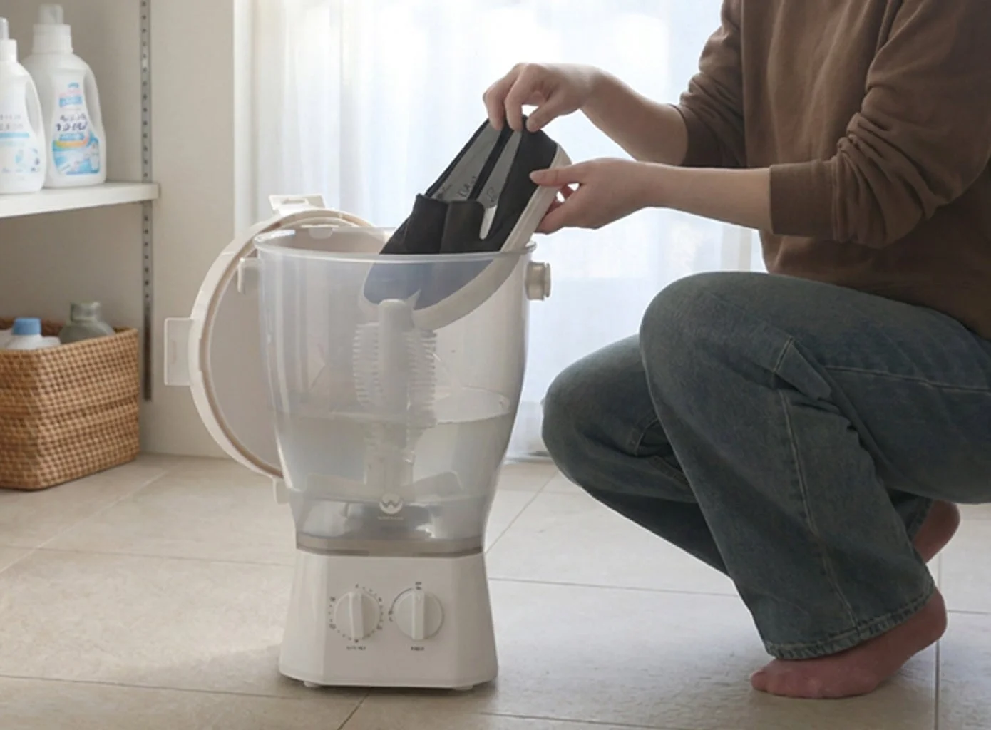 女性がしゃがみ込み、黒いスリッポンシューズを小型の靴用洗濯機に入れている