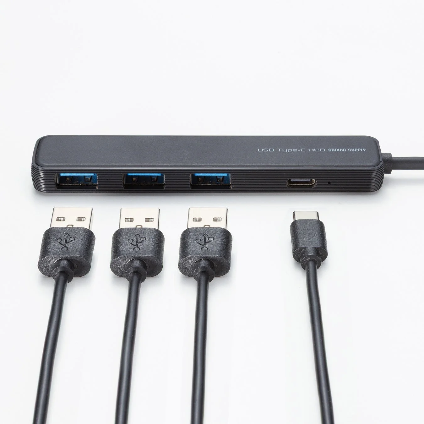 「USB Type-C HUB SANWA SUPPLY」と印字された黒いUSB Type-Cハブと、複数のUSBケーブルが白い背景に置かれている写真。ハブには3つのUSB-Aポートと1つのUSB Type-Cポートが見えます。
