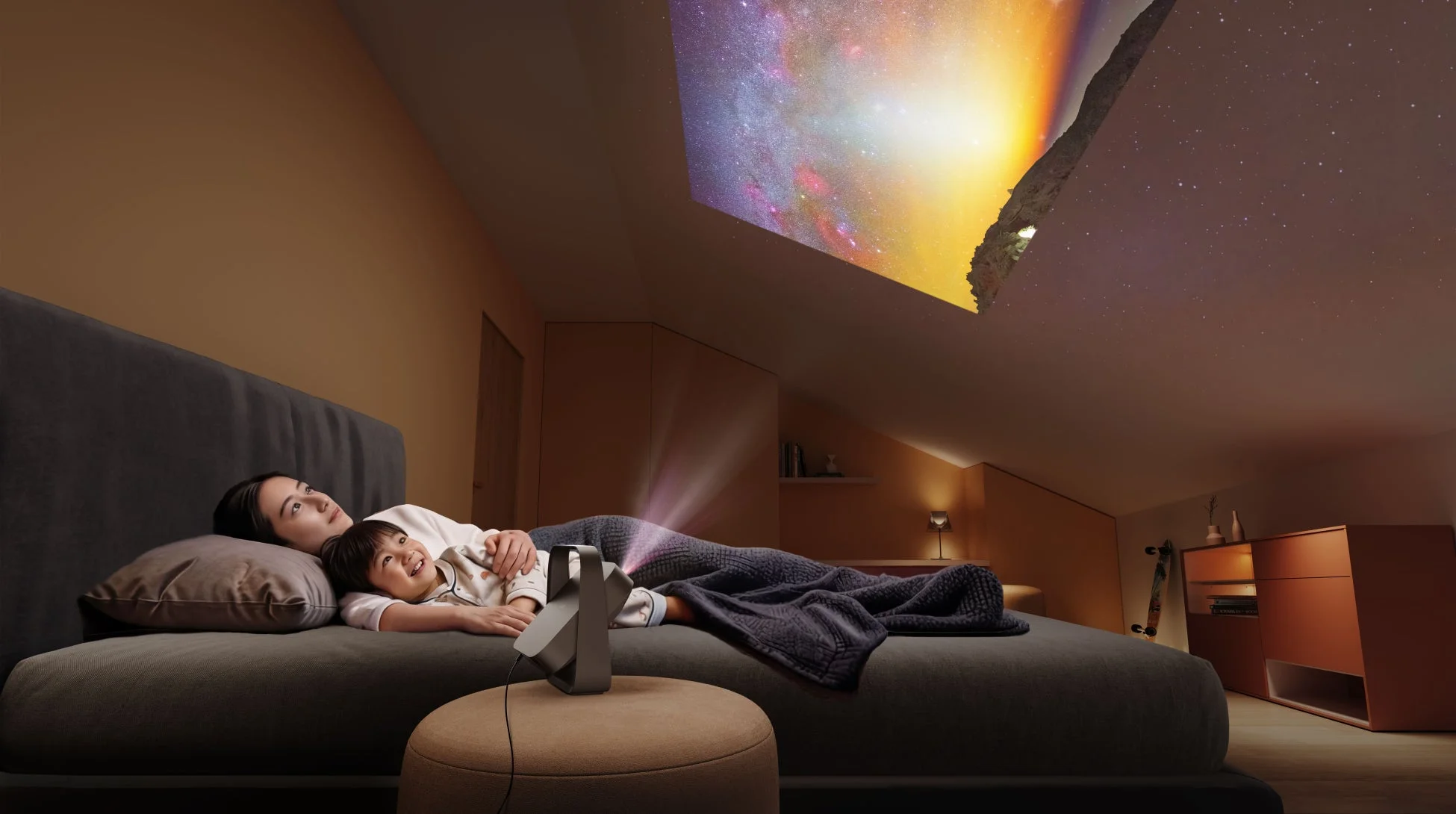 薄暗い寝室のベッドに横たわる母親と子供が、プロジェクターで斜めの天井に映し出された美しい宇宙の映像を眺めている
