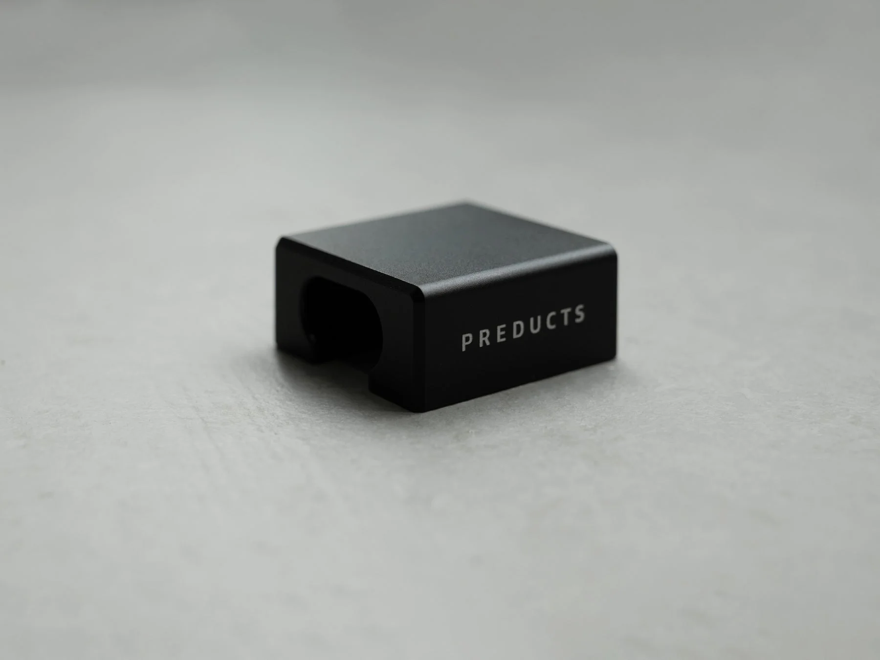 「PREDUCTS」と書かれた黒いミニマルな四角いブロック状の物体が、明るいグレーの背景に置かれている画像です。