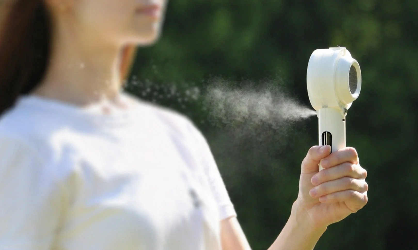 屋外で白い携帯型ミストファンを使用する女性