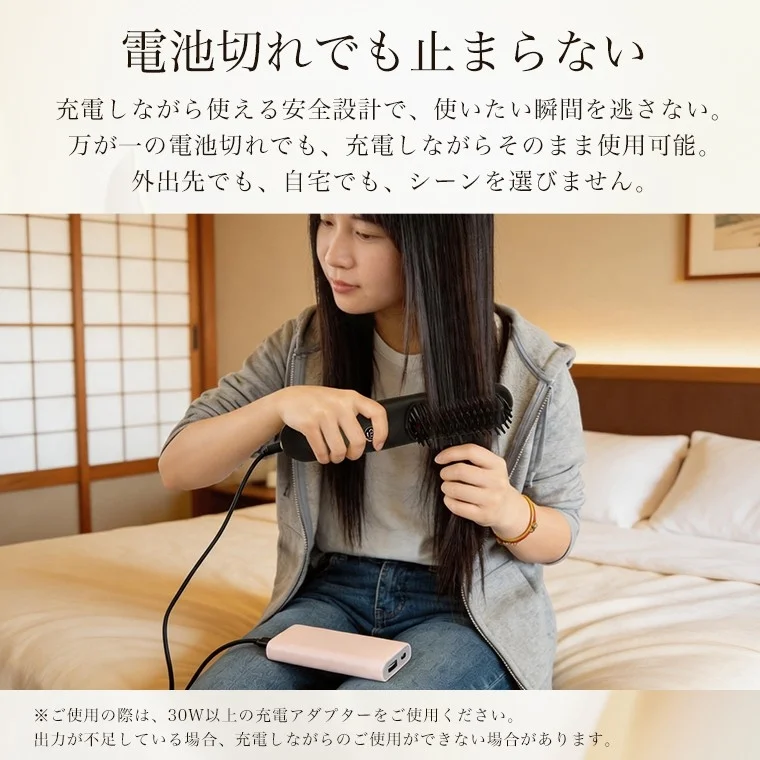 ベッドに座った女性が、充電しながら使えるヘアブラシ型のスタイリングツールを使用しています