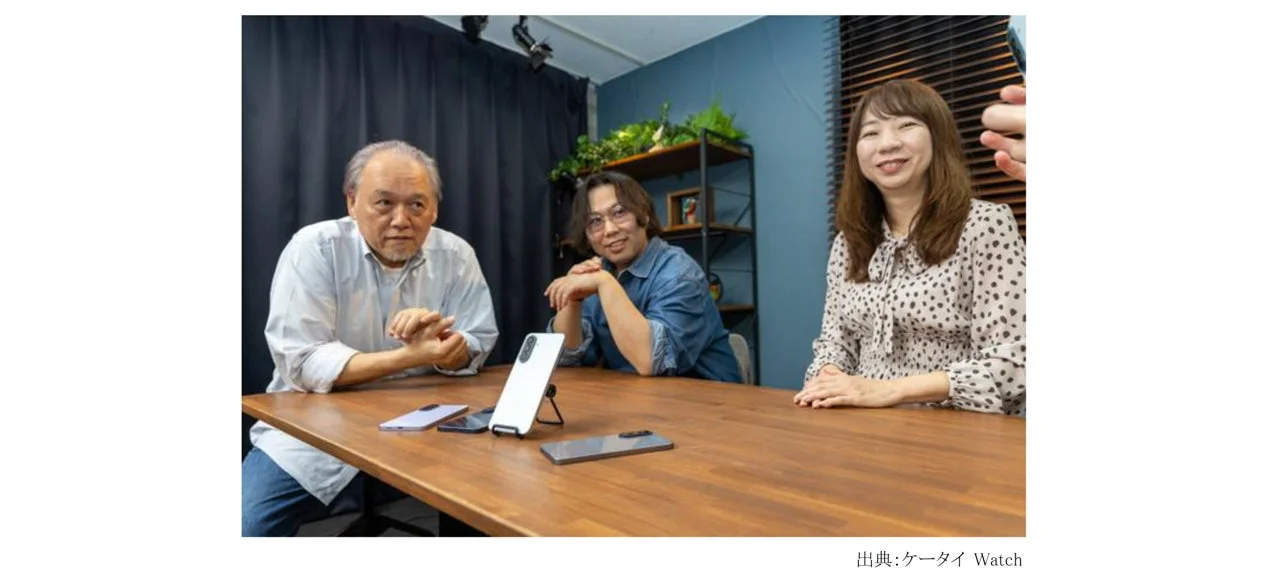 木製のテーブルを囲んで座る3人の男女が写っています。テーブルの上には複数のスマートフォンが置かれています