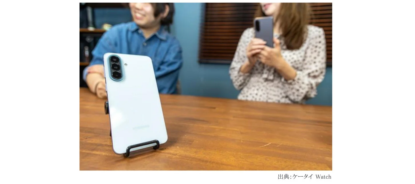 白いスマートフォンがスタンドに立てられ、木製のテーブルの上に置かれている