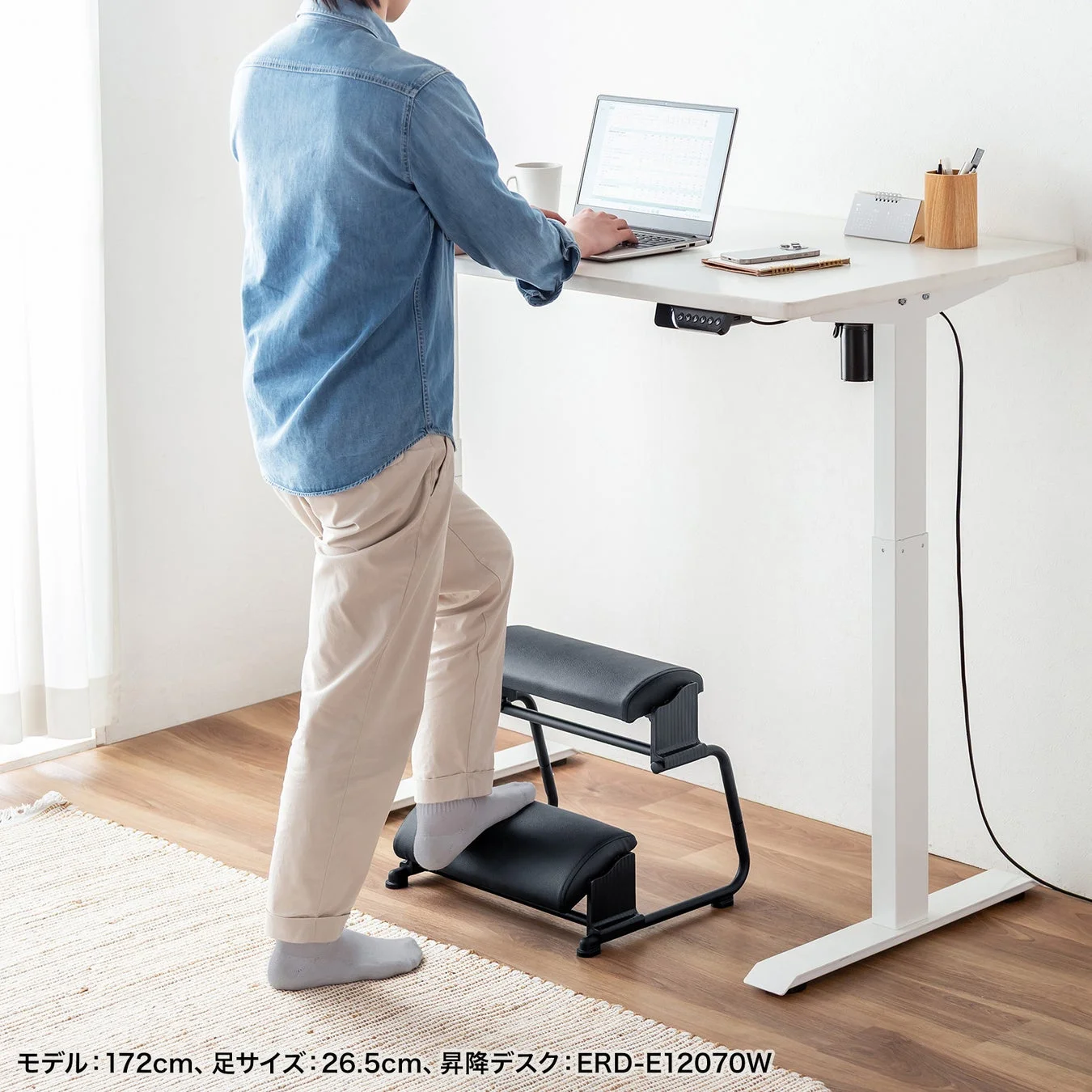昇降デスクで立ち作業中に足置きを使用する男性