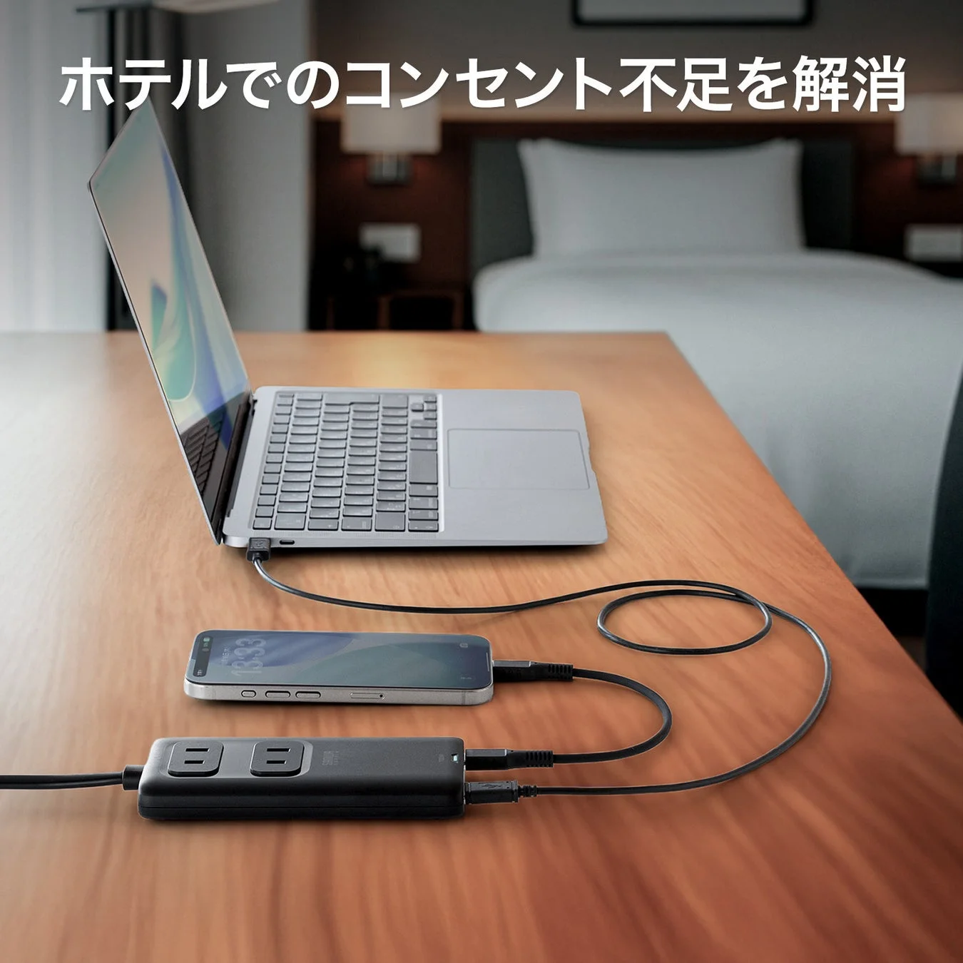 ホテルの一室で、ノートパソコンとスマートフォンが電源タップに接続されています。ホテルでのコンセント不足を解消する様子を示しており、旅行や出張時の充電問題を解決する製品の使用シーンです。