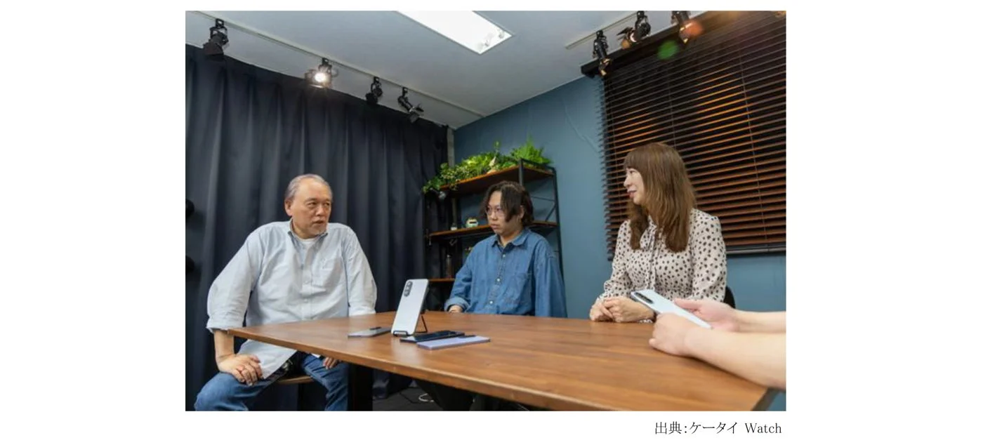 室内で3人の男女がテーブルを囲んで座り、スマートフォンを前に会話している様子