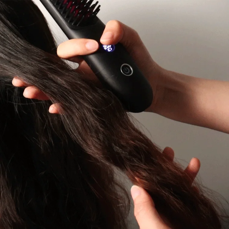 女性が黒いヘアアイロンブラシを使って、長く黒い髪をとかし、ストレートに整えている様子