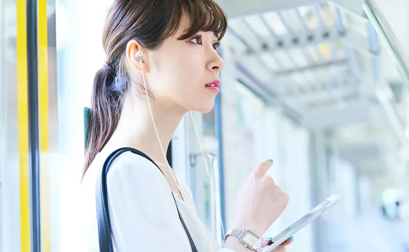 電車内でイヤホンを装着し、スマートフォンを操作している若い女性の横顔を捉えた画像