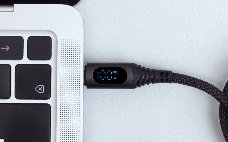 ノートパソコンに接続されたUSB-C充電ケーブルのクローズアップです。ケーブルには「100 PD W」と表示されたデジタルディスプレイがあり、パワーデリバリー対応の100W充電中であることが示されています。