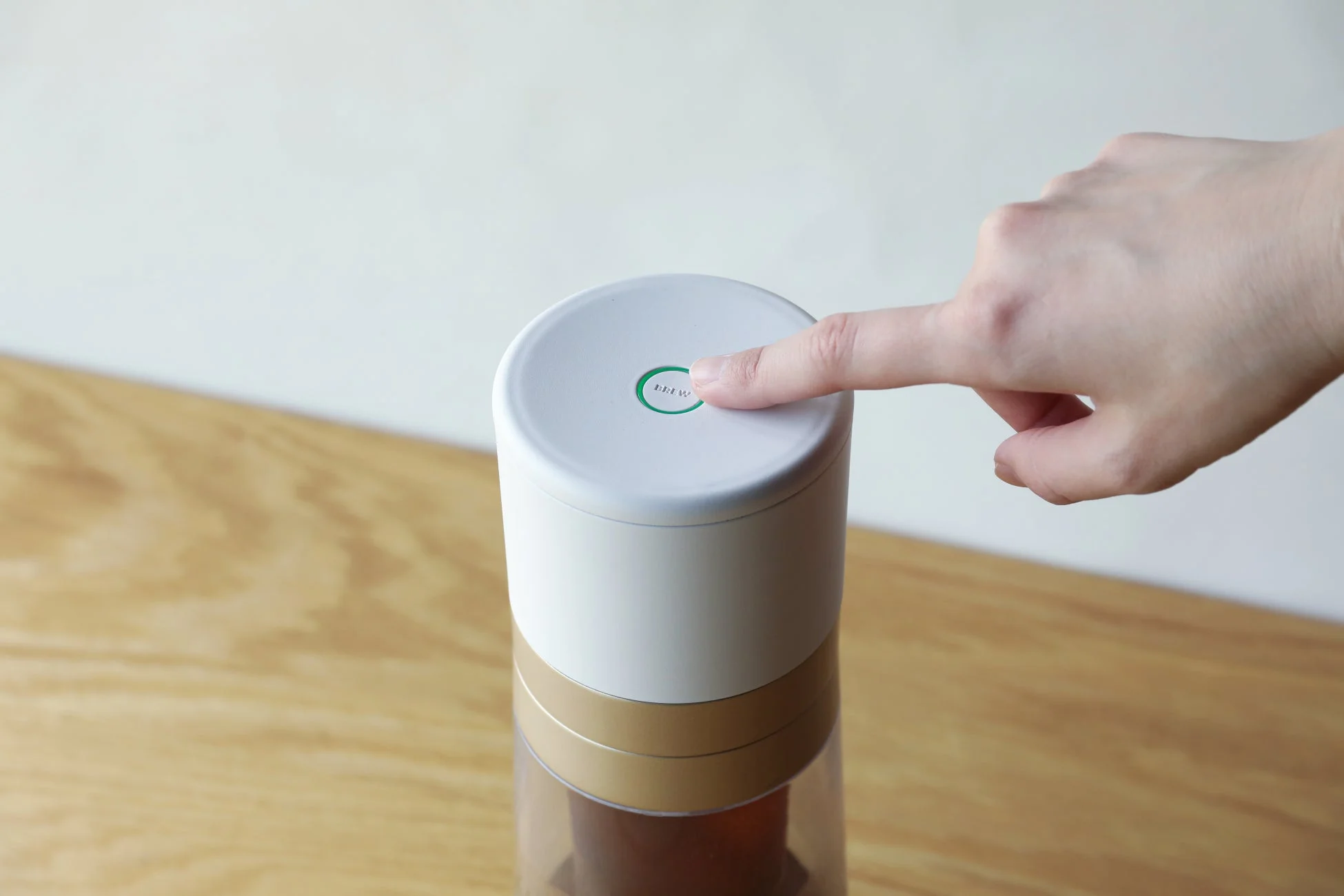 白とゴールドのモダンなデザインの抽出器の天面にある「BREW」ボタンを指で押している様子