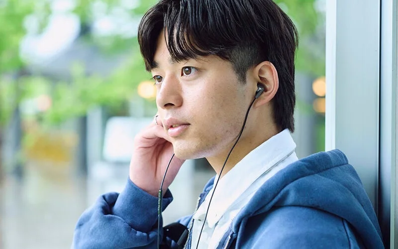男性がイヤホンを使いながら窓の外を見つめている