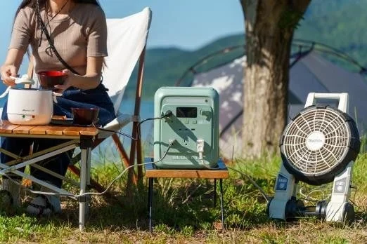 キャンプ場で女性がポータブル電源と家電を使い、食事を楽しんでいます。