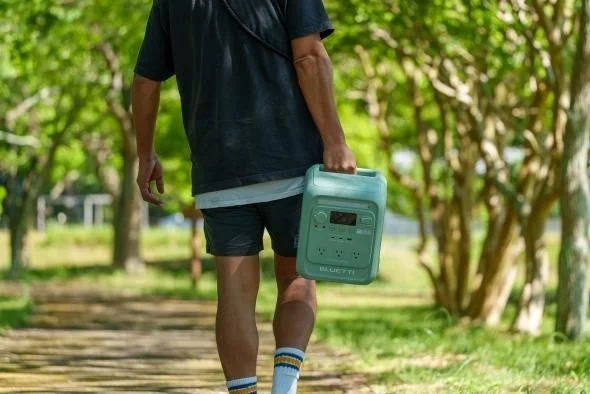 緑豊かな公園の道を歩く男性が、ミントグリーンのポータブル電源を手に持っている様子。
