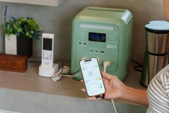 リビングのような空間で、緑色のポータブル電源に接続されたスマートフォンを操作している様子。