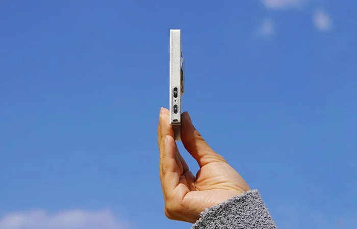 青空を背景に薄型デバイスを持つ手