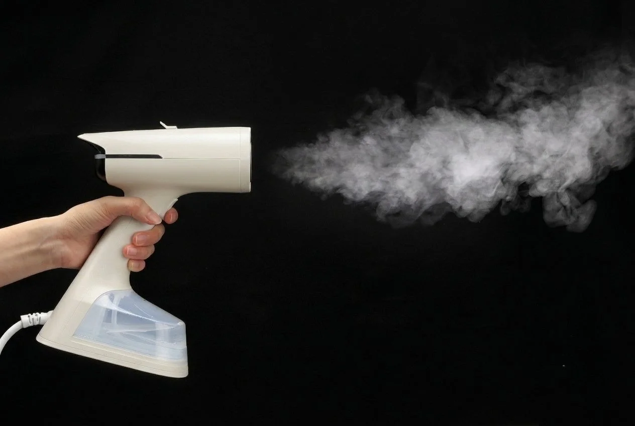 蒸気を噴射する白いハンディ衣類スチーマー