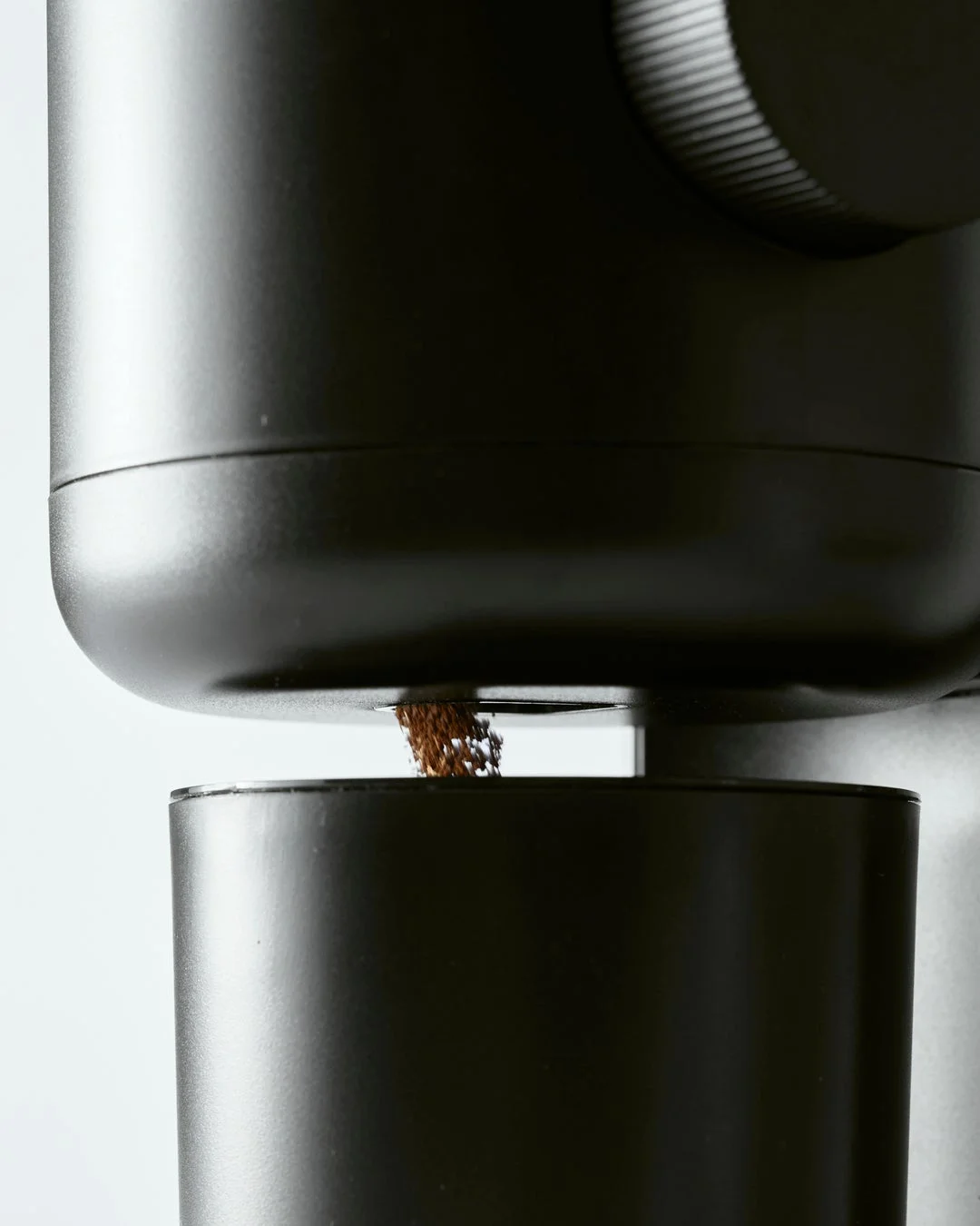 黒いコーヒーグラインダーから挽きたてのコーヒー粉が落ちる様子