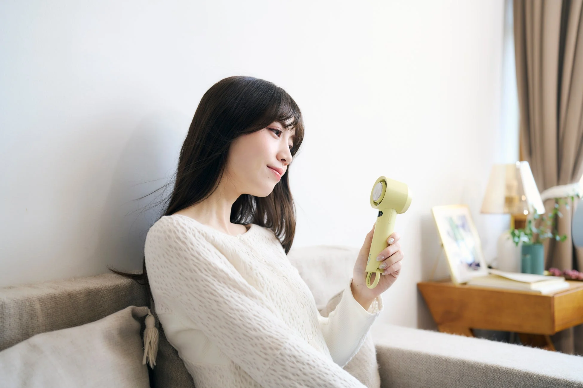 ソファに座り、ハンディファンを使う女性