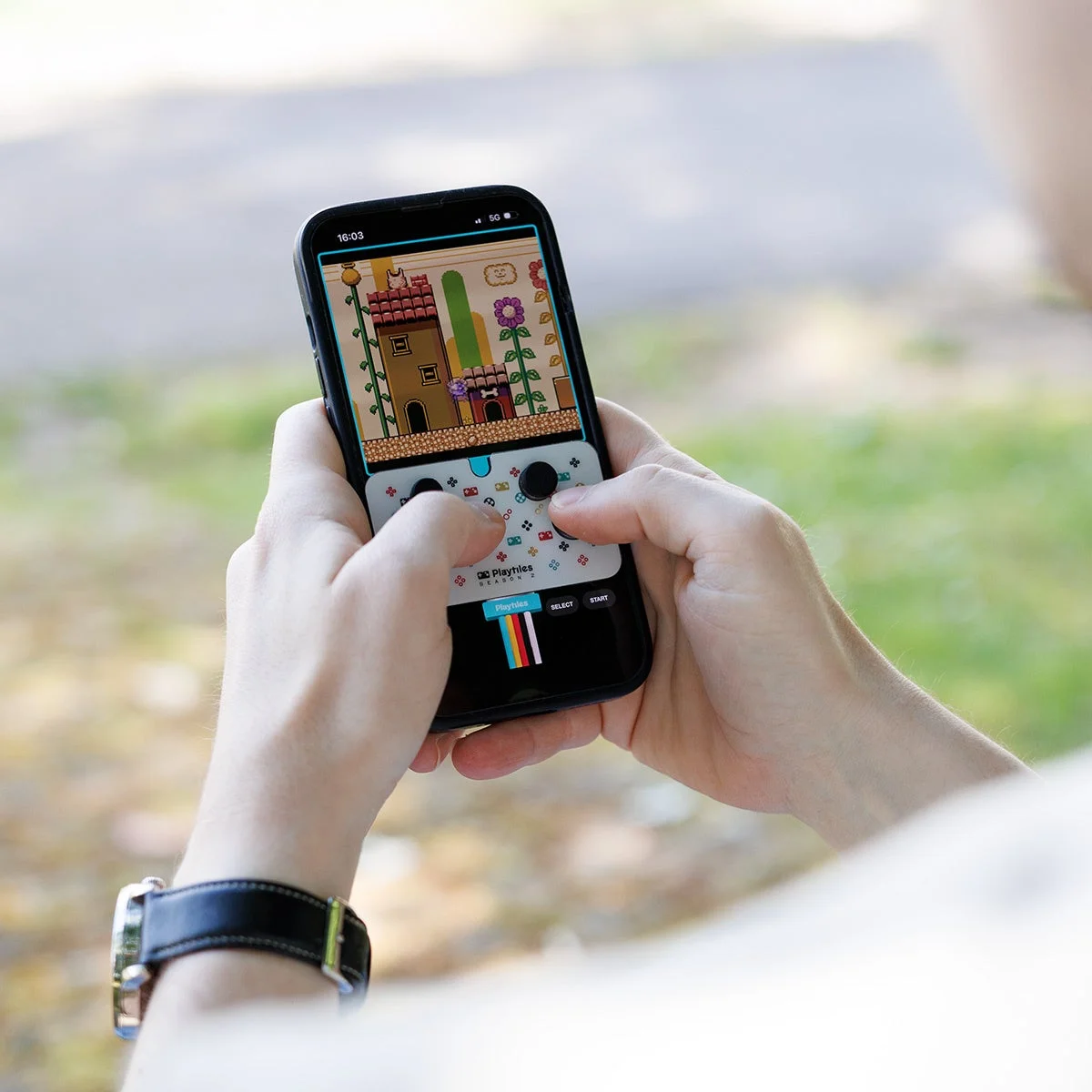 屋外でスマートフォンを操作し、ピクセルアートのレトロ風ゲームをプレイしている様子