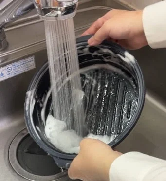 人がキッチンシンクで黒い鍋を洗っている様子