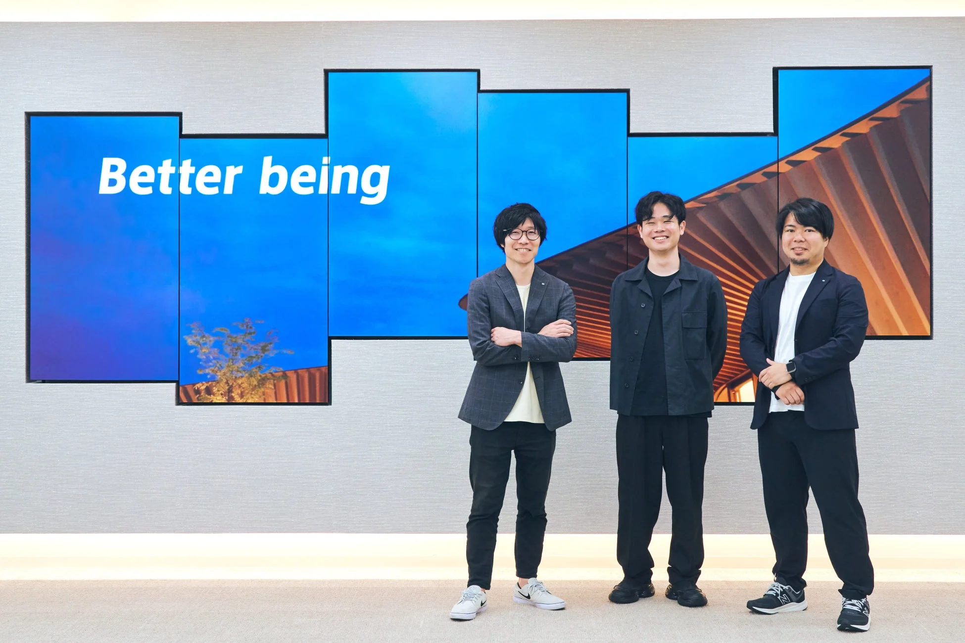 Better beingと表示されたディスプレイを背景に立つ3人の男性
