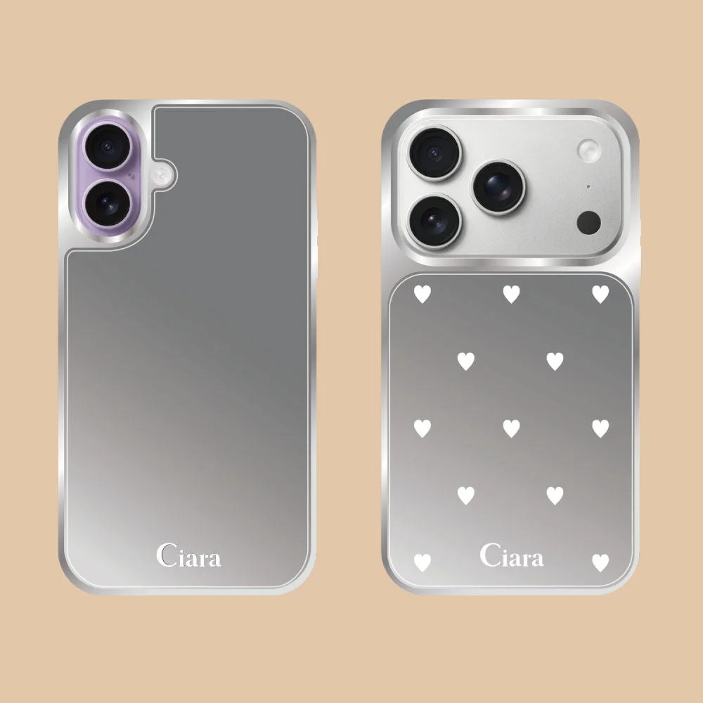 銀色のメメタリックな光沢を持つ2種類のiPhoneケースが写っています。左はシンプルなデザイン、右は白いハート柄が特徴で、どちらにも「Ciara」の文字があります。異なるカメラ形状から、複数のiPhoneモデルに対応していると見られます。