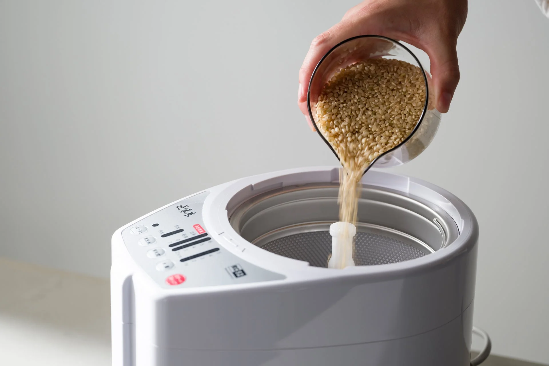白い精米機に玄米を注ぐ手