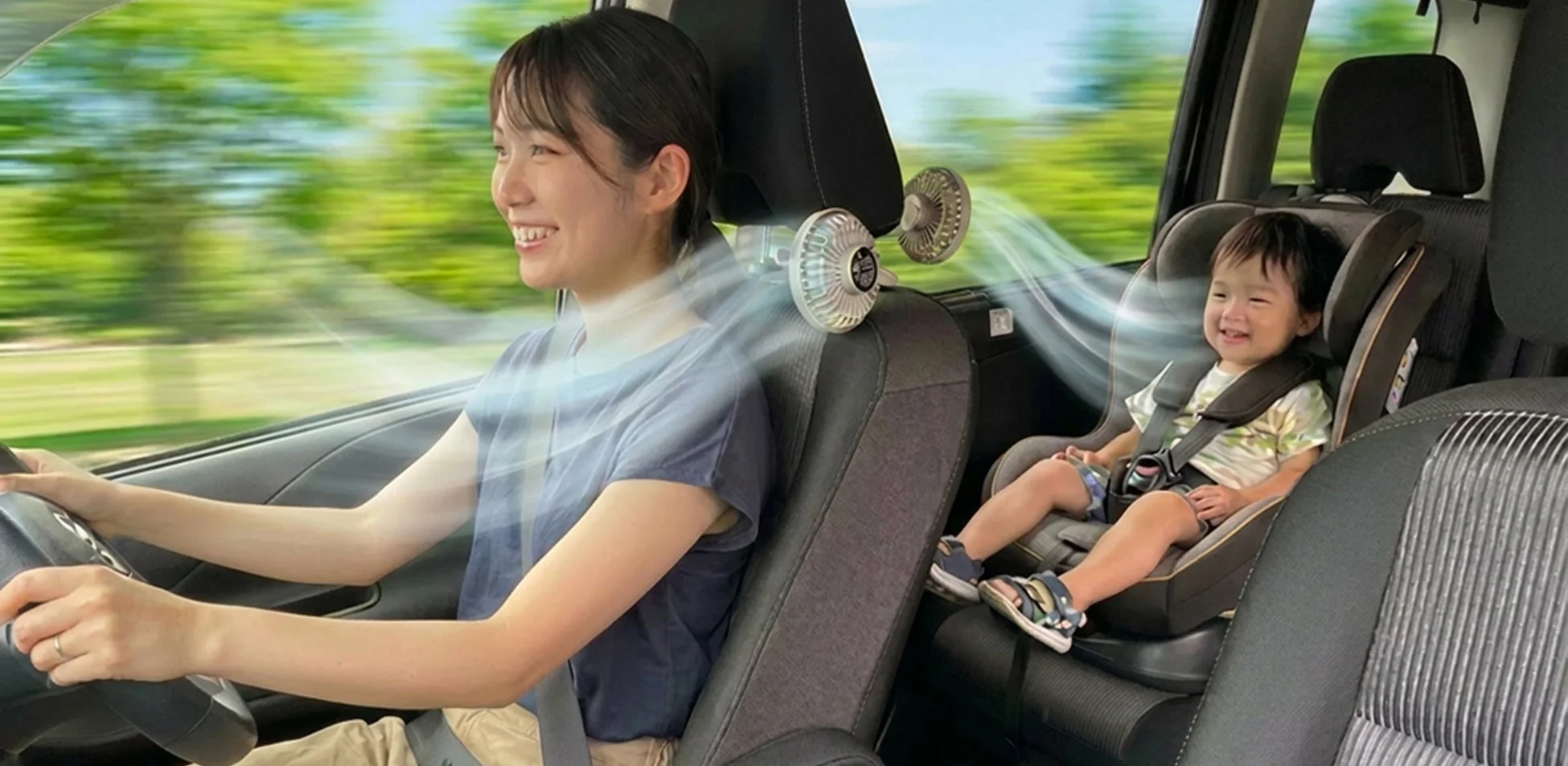 車内で扇風機の風を受けて笑顔の親子の様子