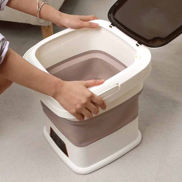 折りたたみ式のフットバスを操作している様子です。蓋つきで、クリーム色と茶色のツートンカラーが特徴。コンパクトに収納でき、自宅での足湯やリラックスタイムに便利です。